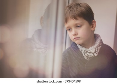 Sad Thoughtful Little Boy Looking Through The Window. Rainy Day