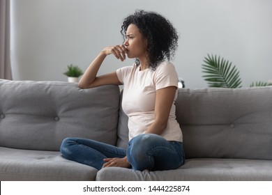 Sad Thoughtful Worried African American Girl Sit On Sofa Looking Away Feel Depressed Doubtful, Lonely Stressed Upset Young Black Girl Thinking Of Psychological Problem Thinking Regret About Mistake