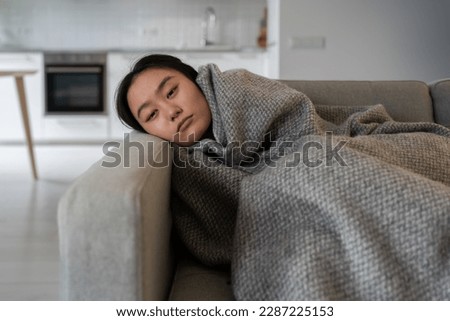Sad tired Asian girl lying alone feels depression apathy indifference to everything melancholy attack has mental problems. Unhappy woman warming wrapped with plaid from central heating problem at home Imagine de stoc © 