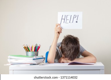 Sad tired frustrated boy sitting at the table with many books and holding paper with word Help. Learning difficulties, education concept.
