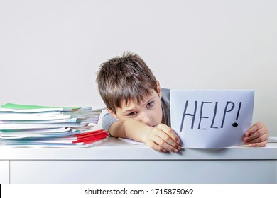 Sad Tired Frustrated Kid Sitting At The Table With Many Books And Holding Paper With Word Help. Learning Difficulties, Education, Online Learning, School At Home