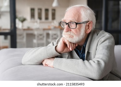Sad tired ill sick lonely disappointed caucasian old elderly senior man grandfather sitting on the sofa couch, feeling nostalgy, pain, missing grandchildren, bankruptcy, fraud at home