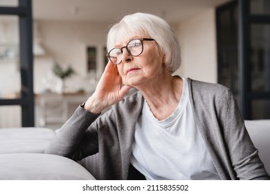 Sad tired ill sick lonely disappointed caucasian old elderly senior woman grandmother sitting on the sofa couch, feeling nostalgy, pain, missing grandchildren, bankruptcy, fraud at home