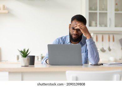 Sad tired unhappy depressed millennial african american bearded male in glasses working on laptop in minimalist white kitchen interior. Deadline, overwork, problems at job and stress, free space - Powered by Shutterstock