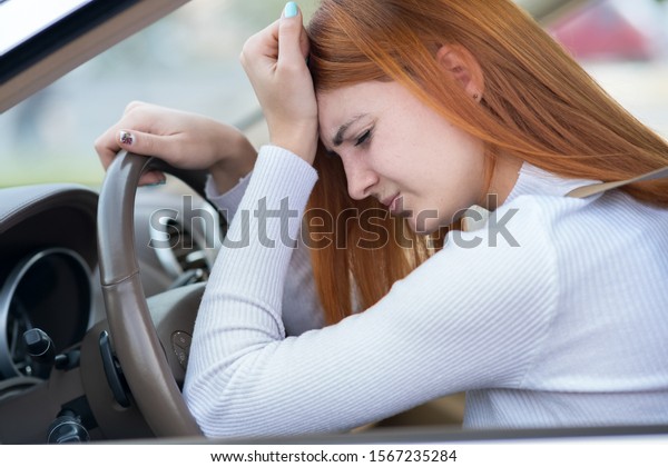 Sad tired yound woman driver sitting behind\
the car steering wheel in traffic\
jam.