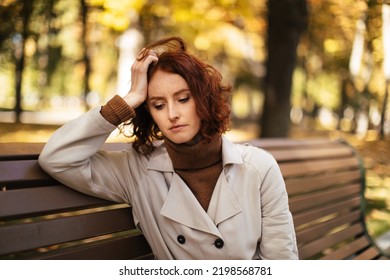 Sad tired young european lady in raincoat sits on bench, thinks, suffer from headache and migraine in park in autumn. Emotions, health care problems, stress and pressure during covid-19 quarantine - Shutterstock ID 2198568781