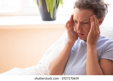 Sad tired young woman massaging temples touching aching head feeling strong headache or migraine, sitting on sofa at home. Suffering from pain or dizziness, feeling depressed doubtful. Copy space