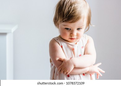 Sad toddler baby girl looking down with her arms crossed