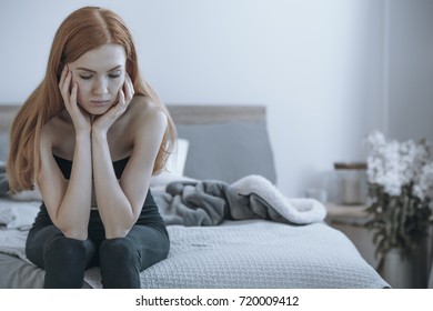 Sad, Underweight Woman Sitting On A Bed Supporting Her Head On Her Hands