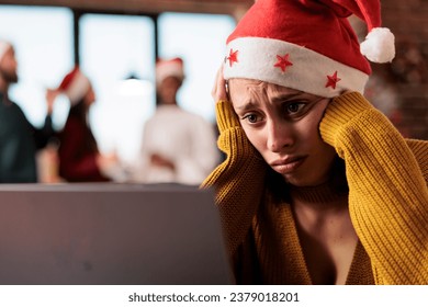 Sad unhappy caucasian woman wearing santa hat working on laptop in office at christmas holiday eve. Exhausted company employee solving task on computer during new year season - Powered by Shutterstock