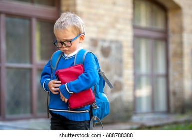 Sad And Unhappy Child With Book In Hands And Backpack. Upset Toddler Boy. Problem Child. Concept For Bullying, Depression Stress Or Frustration. On School Background. Education For Small Kids.