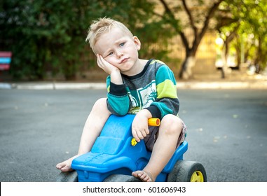 Sad And Unhappy Child On Toy Car Covered His Ear With His Hand. Upset, Angry Toddler Boy. Problem Child With Head In Hands. Concept For Bullying, Depression Stress Or Frustration. Space For Text.