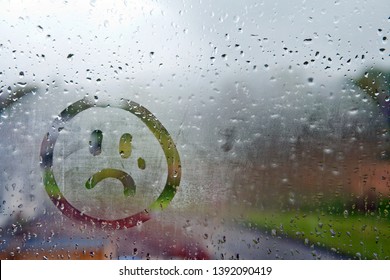 Sad unhappy face drawn on fogged glass on a wet rainy grey window soft light grey skies - Shutterstock ID 1392090419