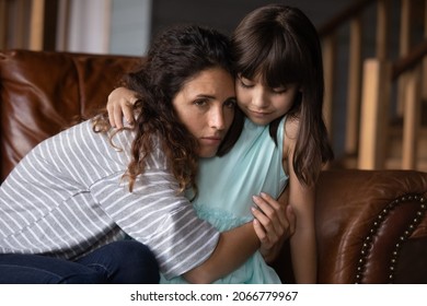 Sad Unhappy Latin Mom Feeling Depressed, Frustrated, Upset, Hugging Daughter Girl On Couch At Home. Young Mother And Kid Facing Problems, Crisis, Loss, Kid, Bad News. Motherhood, Family Support