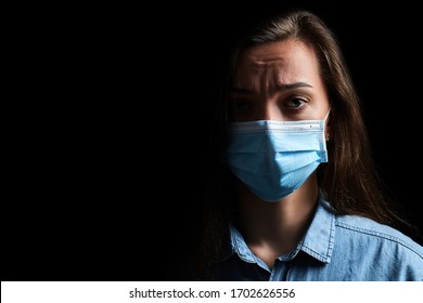 Sad Unhappy Upset Woman In Protective Medical Mask On A Black Background. Health Protection During Covid Ncol Flu Epidemic And Air Pollution. Copy Space    