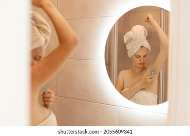 Sad Unhappy Young Adult Woman Shaving Armpit In Bathroom, Looking At Her Body, Depilation Process, Attractive Female With Bare Shoulders And Wrapped In White Towel.