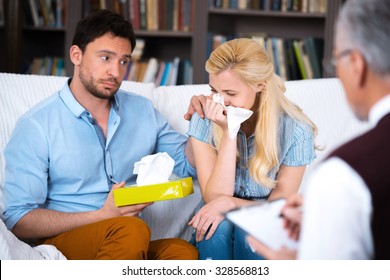 Sad unhappy young couple talking with psychologist. Psychologist taking notes. Woman crying. There are many books in psychologist office