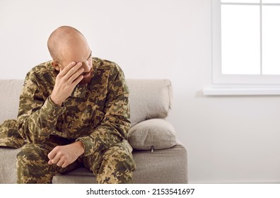 Sad Upset Depressed Veteran Soldier Suffering From PTSD Sitting On Couch At Home In His Military Uniform And Thinking About Horrors Of War. Trauma, Post Traumatic Stress Disorder Concept