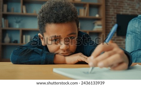 Sad upset lazy unmotivated tired exhausted fatigued little African American pupil schoolboy writing notes write homework task lying on table. Ethnic child boy kid son at desk boring class home lesson