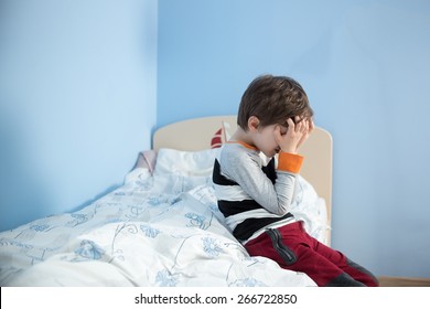 Sad, Upset Little Boy Sitting On The Edge Of His Bed. Covering His Face With Hands.