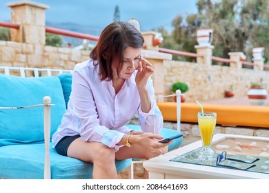 Sad Upset Mature Woman Sitting Outdoors At Table In Cafe With Smartphone