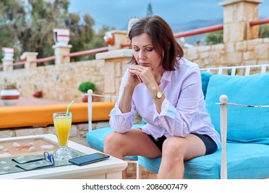 Sad Upset Mature Woman Sitting Outdoors At Table In Cafe With Smartphone