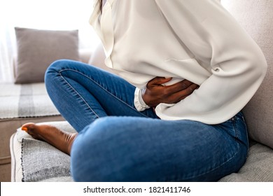 Sad, Upset, Unhappy Woman Holding Hands On Stomach Suffering From Abdominal Pain With Close Eyes, Having Menstrual Period, Food Poisoning, Gastritis, Diarrhea, Feeling Unwell Sitting In Livingroom