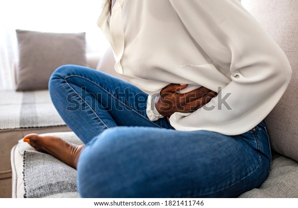Sad, upset, unhappy woman holding hands on\
stomach suffering from abdominal pain with close eyes, having\
menstrual period, food poisoning, gastritis, diarrhea, feeling\
unwell sitting in\
livingroom