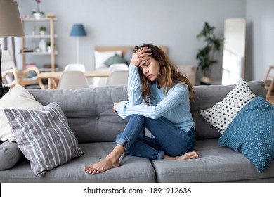 Traurige verärgerte Frau sitzt allein im Wohnzimmer auf dem Sofa, psychologisches Problem. 