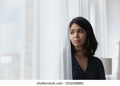 Sad Upset Young Asian Woman Stand By Window Hide Behind Curtain Look Aside Think Of Heartbreak Loneliness. Frustrated Teenage Female Having Problems Suffer Of Misunderstanding Depression. Copy Space