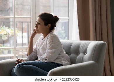 Sad upset young Indian woman thinking while sit on armchair and staring out window. Personal troubles and break up, goes through difficult life situation, search solution, ponders seated alone at home - Shutterstock ID 2222360625