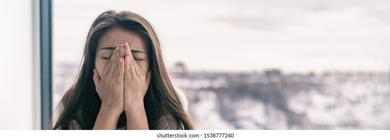 Sad upset young woman crying with mental health seasonal affective disorder at home breathing in hands panoramic background banner. Winter blues.
