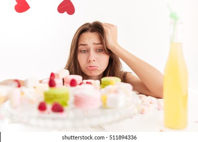 Sad Upset Young Woman Looking At Sweests On The Table