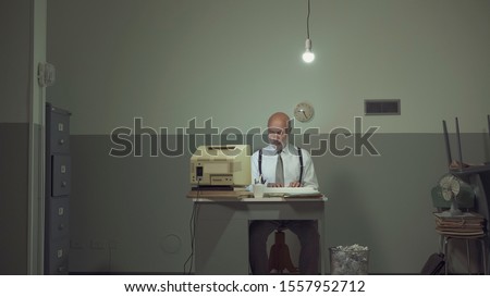 Sad vintage style businessman working in a small rundown office with an outdated computer, he feels frustrated and disappointed