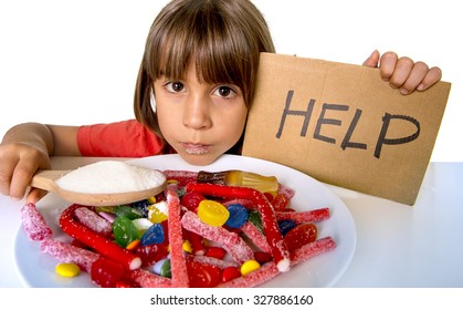 sad and vulnerable 4 or 5 years old female child asking for help  eating dish full of candy holding sugar spoon in sweet abuse dangerous diet and unhealthy nutrition concept isolated on white