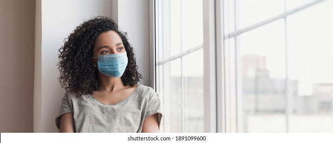 Sad Woman Alone During Coronavirus Pandemic Wearing Face Mask Indoors At Home For Social Distancing. Mixed Race Girl Looking At Window, Banner. Anxiety, Stress, Lockdown, Mental Health Crisis Concept