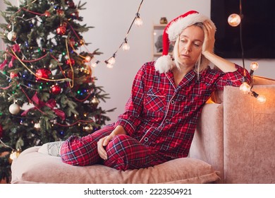 Sad woman by the Christmas tree contemplating. Stressed middle woman in front of Christmas tree. Sad lonely adult girl complaining in Christmas sitting on couch in the living room at home
