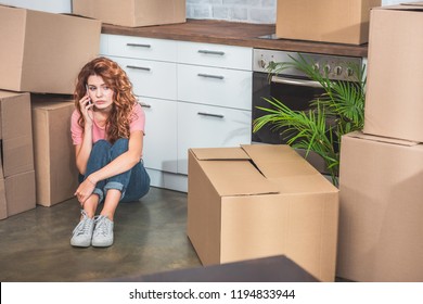 sad woman in casual clothes sitting on floor near cardboard boxes and talking by smartphone at new home - Powered by Shutterstock