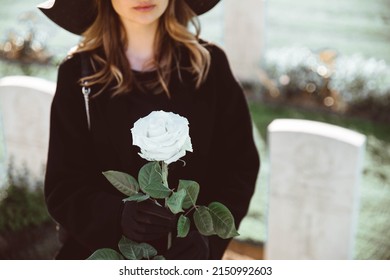 Sad woman in the cemetery holding bouquet of roses in her hand - Powered by Shutterstock