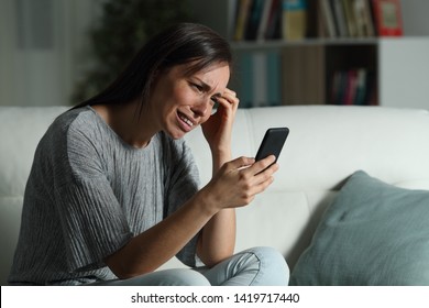 Sad Woman Checking Smart Phone In The Night Sitting On A Couch In The Living Room At Home