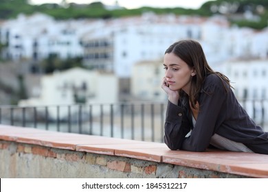 Sad woman complaining alone looking down in a balcony in a town on the beach