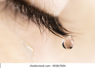 Sad woman concept - closed eyelid closeup with a teardrop on eyelashes.  A tear on eyes macro close-up. A tear runs down his cheek. Tinted beige.