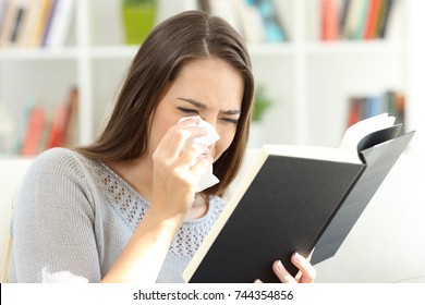 Sad woman crying while is reading a good paper book sitting on a sofa at home