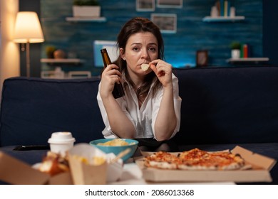 Sad Woman Drinking Craft Beer And Eating Potato Chips From Bowl At Table With Large Pizza And Takeout Dinner In Home Living Room. Tired Office Worker On Couch Relaxing After Takeaway Menu.