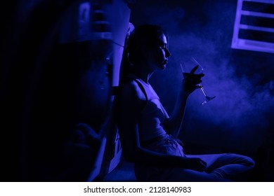 Sad Woman Drinking Wine While Sitting Near The Refrigerator In The Dark.