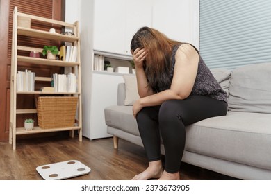 Sad woman with fat upset bored of dieting Weight loss fail  Fat diet and scale sad asian woman on weight scale at home weight control.