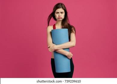 sad woman holding a fitness mat on a pink background                                - Powered by Shutterstock