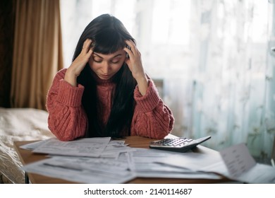 Sad woman holding her head over utility bills. The concept of rising prices for heating, gas, electricity. A young worried dissatisfied girl looks at papers does not expect a high cost of services - Shutterstock ID 2140114687