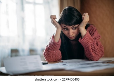 Sad woman holding her head over utility bills. The concept of rising prices for heating, gas, electricity. A young worried dissatisfied girl looks at documents, does not expect a high cost of services - Shutterstock ID 2179405405