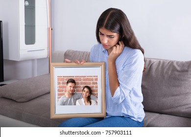 Sad Woman Holding Picture Frame Of Couple In Love At Home